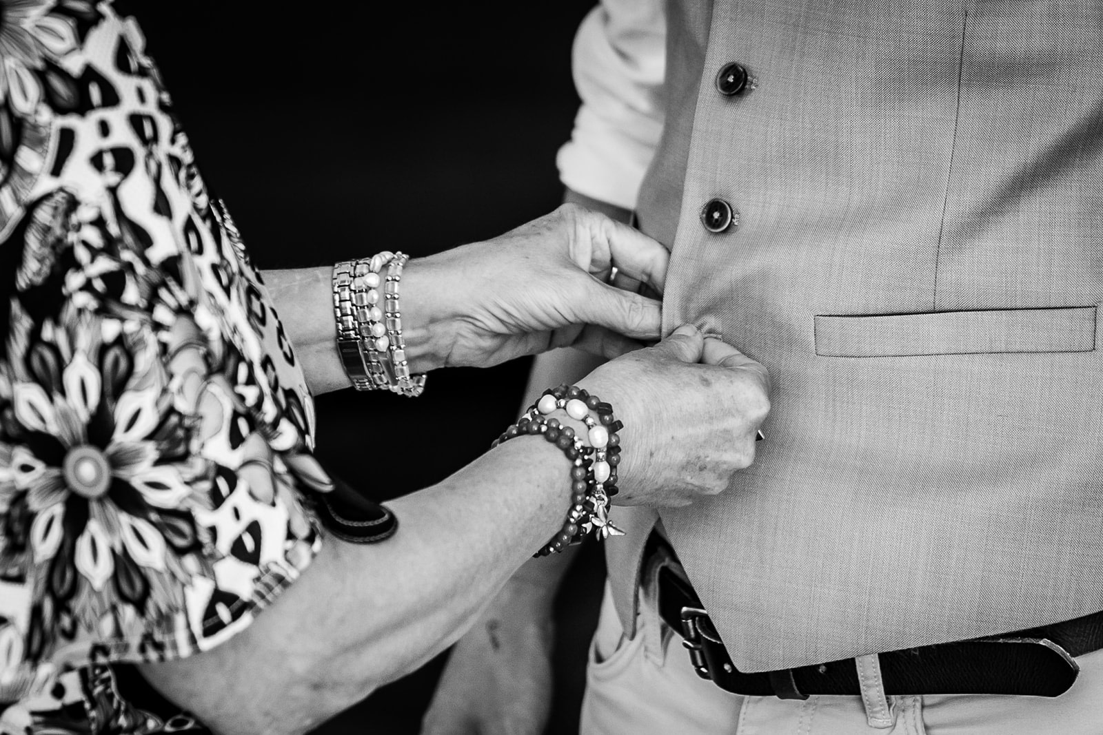 A couple dances closely outdoors, smiling and gazing into each other's eyes. Captured by a natural wedding photographer, the black and white photo features tables and guests in the background, hinting at a joyful celebration.